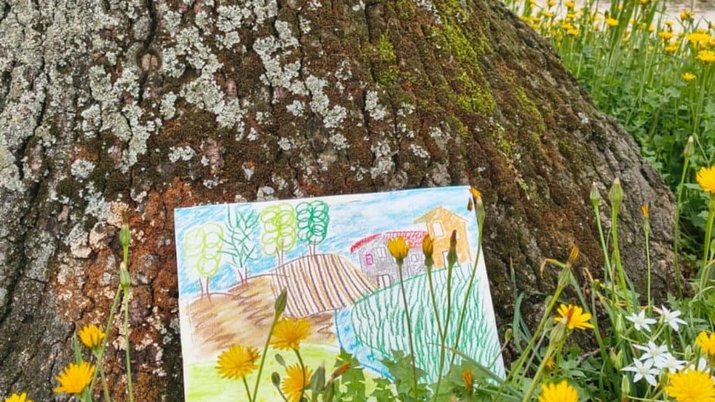 gemaltes Bild steht vor einem Baum in einer Blumenwiese